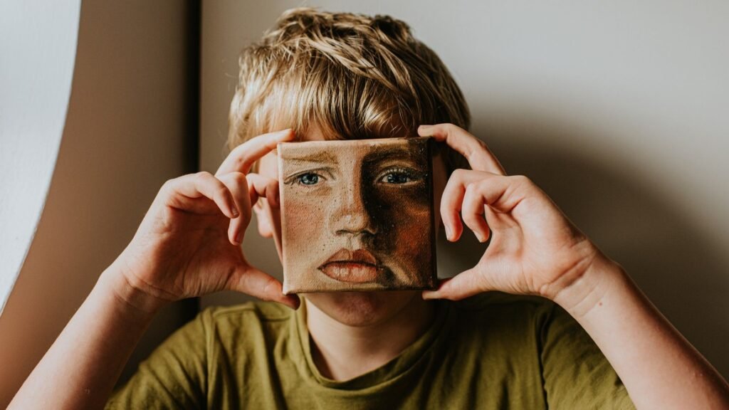 First Grammarly cloned me without permission. Then another AI company asked if it could do the same—for $2,000 A young lad covers his face with a small oil painting of himself. The expression on the painting is serious.