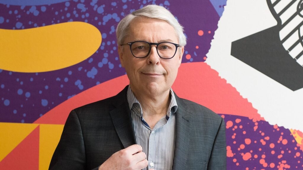 Claude Guillemot, co-founder of Ubisoft, dies in plane crash Claude Guillemot, wearing a suit and glasses, stands in front of a brightly coloured patterned background.